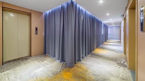 A hotel hallway with a patterned carpet, a blue curtain, and an elevator. - Wanlonghote (Cenxi)