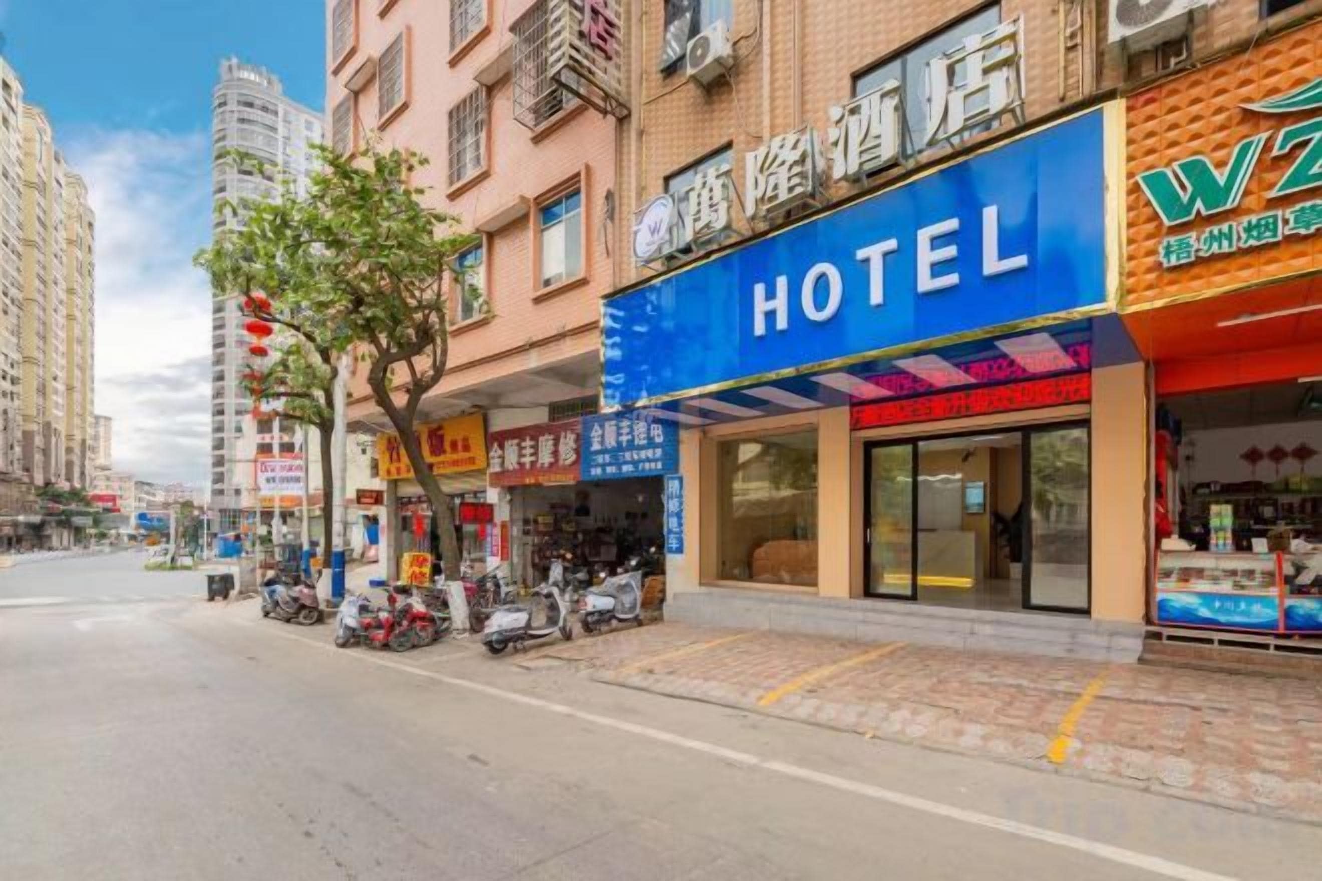 A hotel with a prominent blue sign, a storefront with a red awning, and a row of parked scooters on the sidewalk.