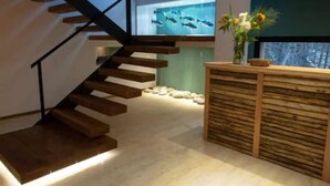A modern interior with a wooden staircase, a reception desk, and a wall-mounted aquarium. - Hotel Alto Traful (Villa Traful)