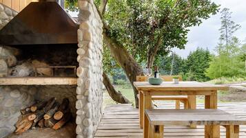 Una chimenea de piedra al aire libre con leña, una mesa de madera y un banco.