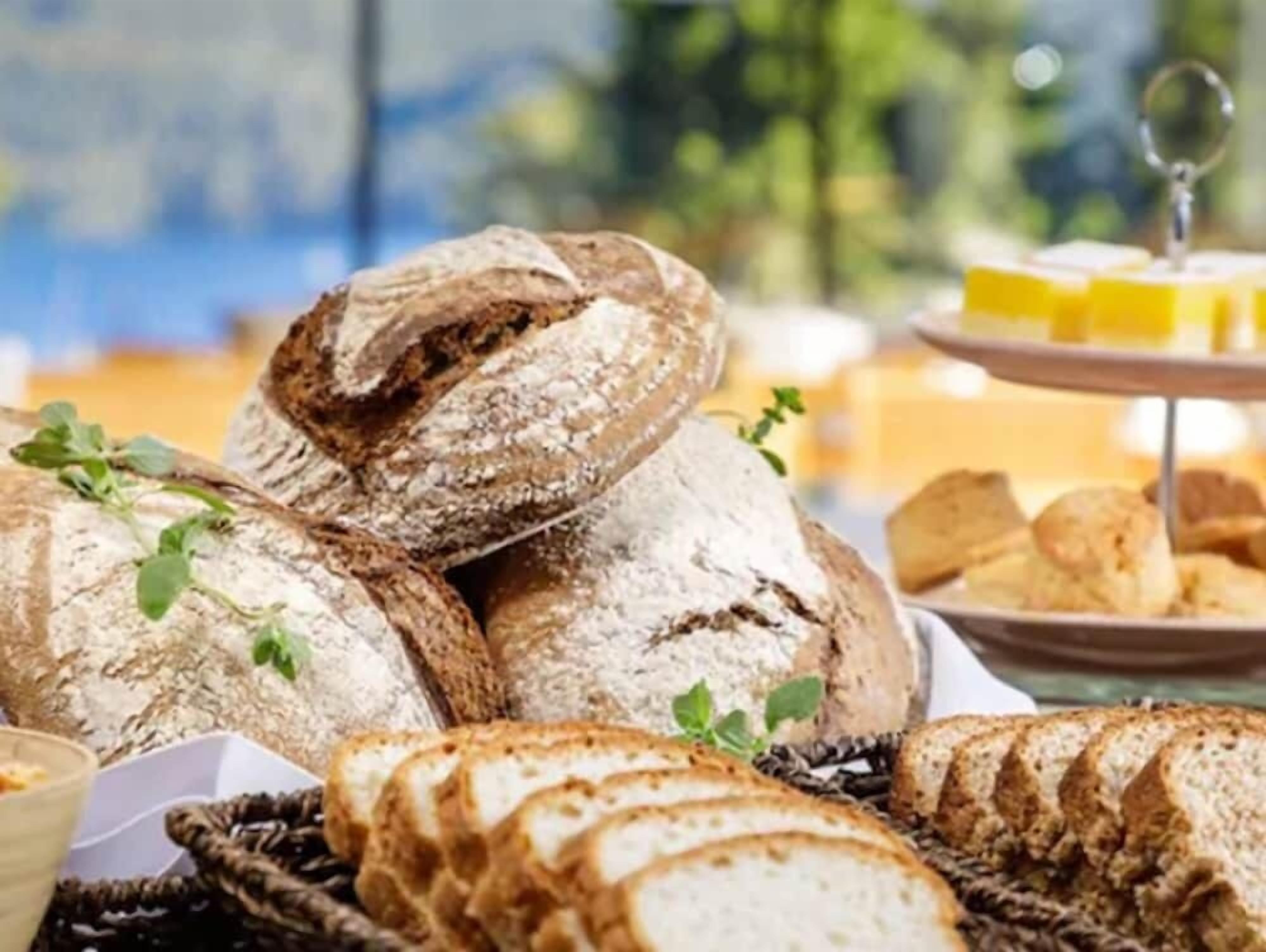 A variety of breads and pastries on a table, including whole and sliced loaves, with a small dish of butter and a container of cream.