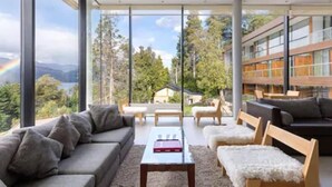 Una sala de estar moderna con un ventanal grande, un sofá, una mesa de centro y vistas a un bosque y montañas.