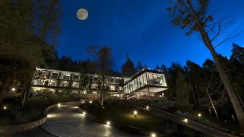 Un edificio moderno de varios pisos con fachada iluminada y un jardín ajardinado.