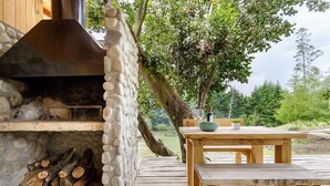 Una chimenea de piedra al aire libre con chimenea, rodeada por una terraza de madera y una mesa con sillas.
