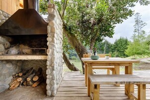 Una chimenea de piedra al aire libre con chimenea, rodeada por una terraza de madera y una mesa con sillas.
