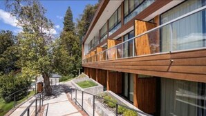 Un edificio moderno con amplios ventanales, fachada de madera y un área ajardinada con un sendero y barandilla.