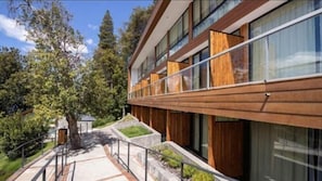 Un edificio moderno con amplios ventanales, fachada de madera y un área ajardinada con un sendero y barandilla.