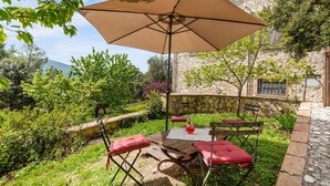 A wooden table with red cushions, a beige umbrella, and a stone wall in the background. - Gorgeous apartment in Loc. Fontanelle with WiFi (Loc. Fontanelle)