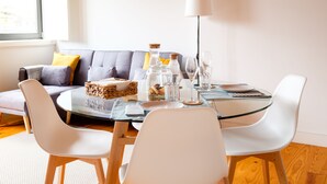 Ein Essbereich mit einem runden Glastisch, weißen Stühlen, einem grauen Sofa mit gelben Kissen und einer Stehlampe.