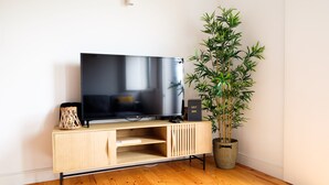 Ein modernes Wohnzimmer mit einem Flachbildfernseher auf einem Holzboden, einer Bambuspflanze und einem Schild mit der Aufschrift 'GUEST BOOK'.