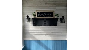 A wall-mounted sign with the text "Welcome to our home" above a black shelf with two potted plants on either side. - Bay View Gem (Milwaukee)