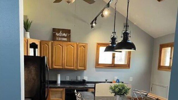 A kitchen with wooden cabinets, a black refrigerator, a dining table with chairs, a ceiling fan, and pendant lights. - Bay View Gem (Milwaukee)