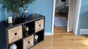 A room with a wooden floor, a black console table with woven baskets, a potted plant, and a white wall with a letter 'M'. - Bay View Gem (Milwaukee)