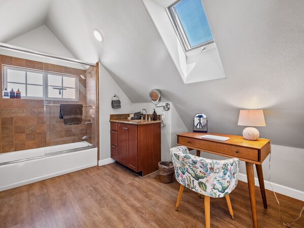 Une salle de bain avec une douche, un meuble-lavabo, un bureau avec une lampe et une chaise.