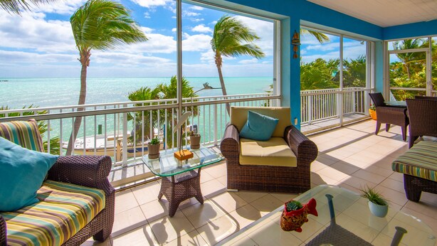 A balcony with wicker furniture, a glass table, and potted plants. - Waterfront Oasis - 3/2 w/ Heated Pool & Direct Ocean Views (Marathon)