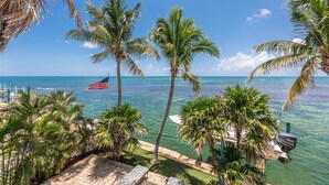 A view of a marina with palm trees, a yacht, and an American flag. - Waterfront Oasis - 3/2 w/ Heated Pool & Direct Ocean Views (Marathon)