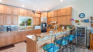 A kitchen with wooden cabinets, granite countertops, a bar area with blue chairs, and a wine rack. - Waterfront Oasis - 3/2 w/ Heated Pool & Direct Ocean Views (Marathon)