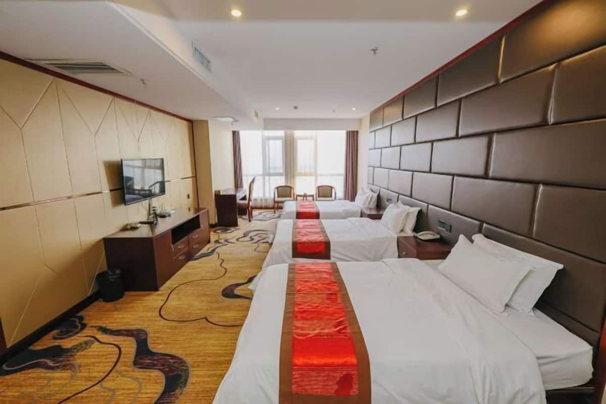 A hotel room with two beds, a TV, a desk, and a large window.