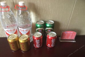 Una mesa con botellas y latas de bebidas, un cartel con el menú y una pared.