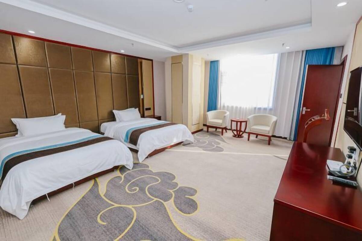 A hotel room with two beds, a desk, a chair, and a large window with curtains.