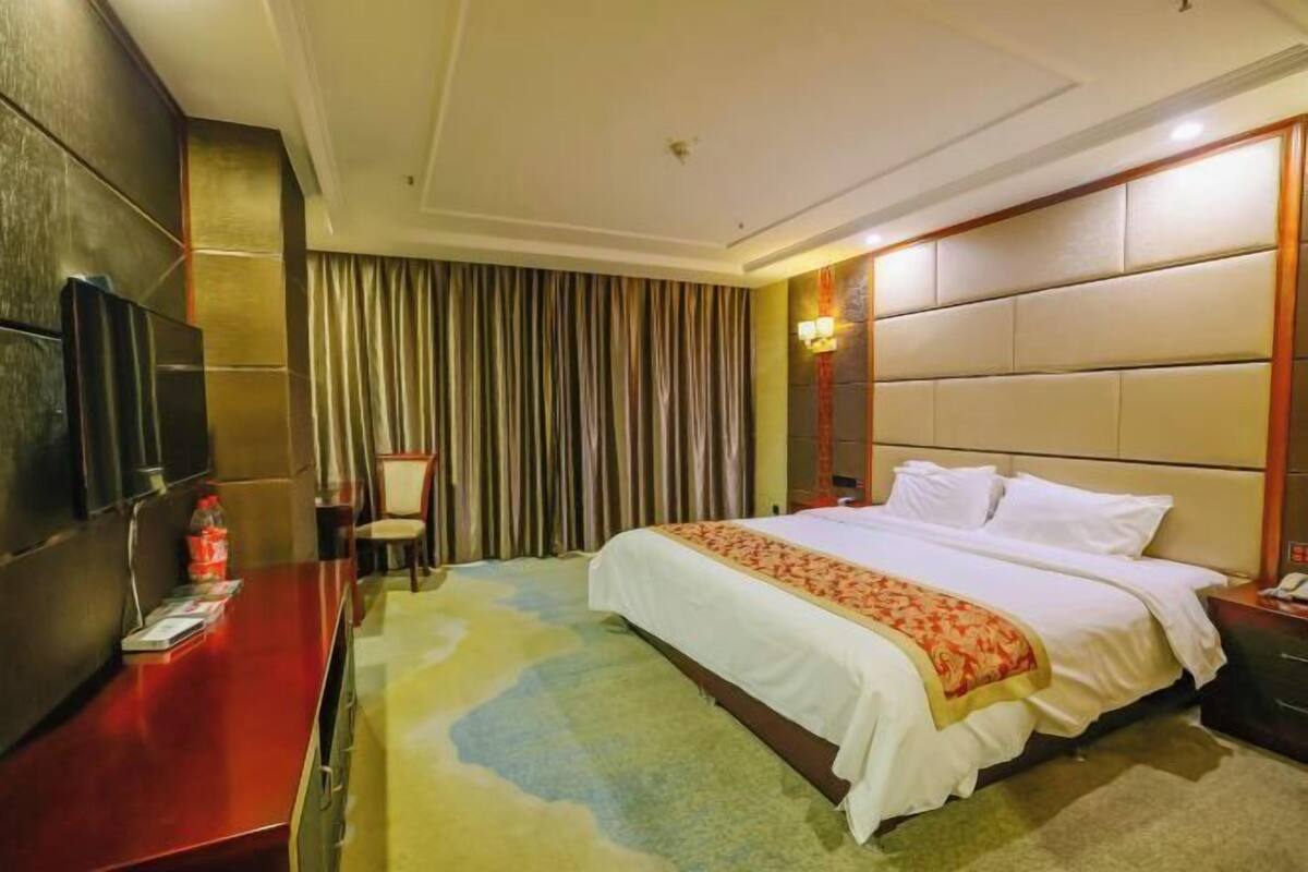A hotel room with a bed, a desk, a television, and a curtain.