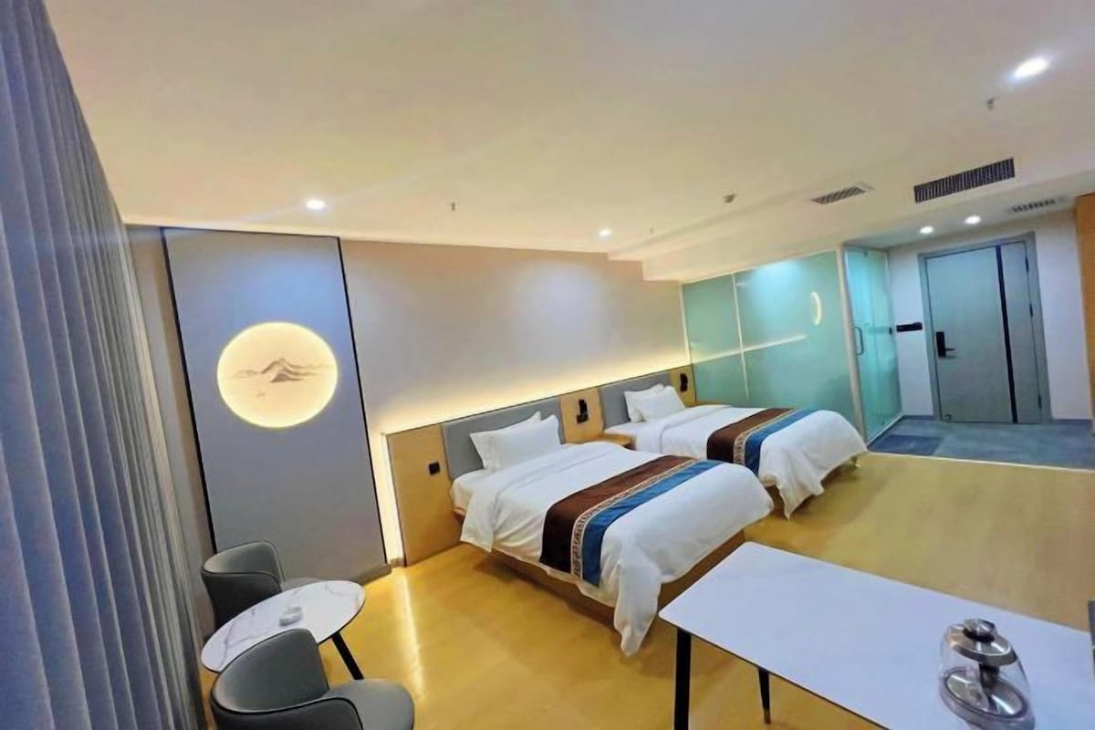 Una habitación de hotel con dos camas, una mesita y un espejo.