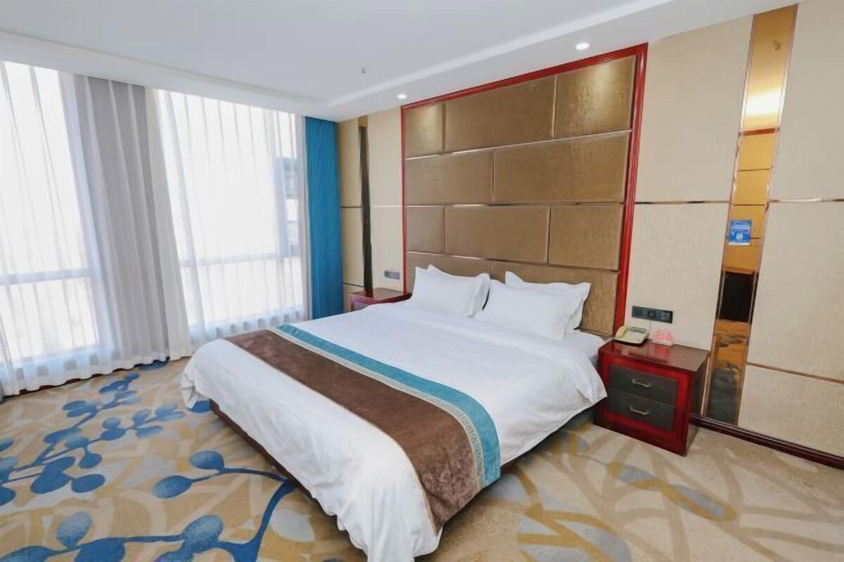 A hotel room with a large bed, a nightstand, a mirror, and a window with curtains.