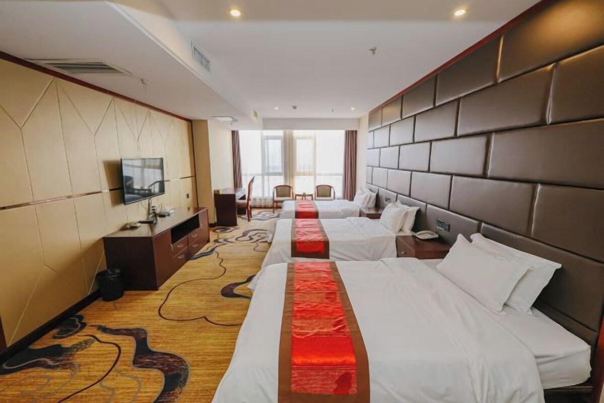 A hotel room with two beds, a TV, a desk, and a large window.