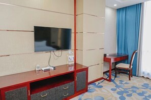 A hotel room with a flat-screen TV mounted on a wall, a wooden desk with a chair, and a patterned carpet. - Boyin Hotel (Jiang County)