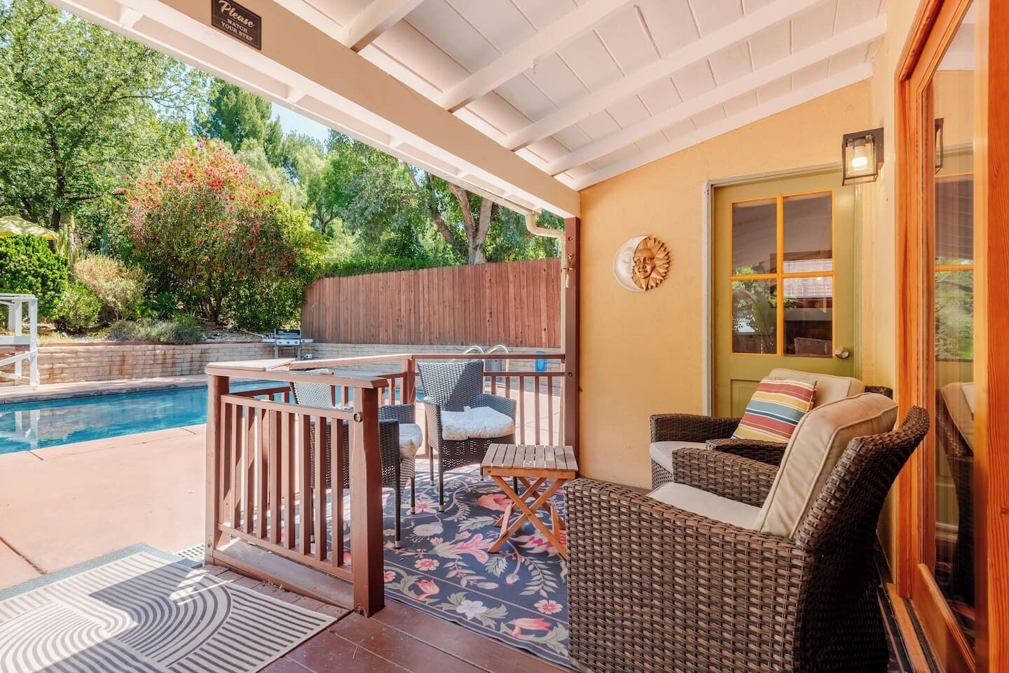 A covered patio with a pool, outdoor furniture, and a view of the surrounding greenery.
