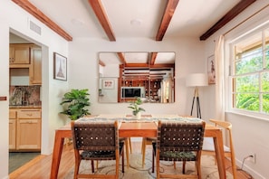 A dining area with a wooden table, two chairs, a mirror, and a window with a view of greenery.