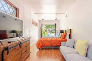 A bedroom with a bed, a sofa, a wooden dresser, a desk, and a window.