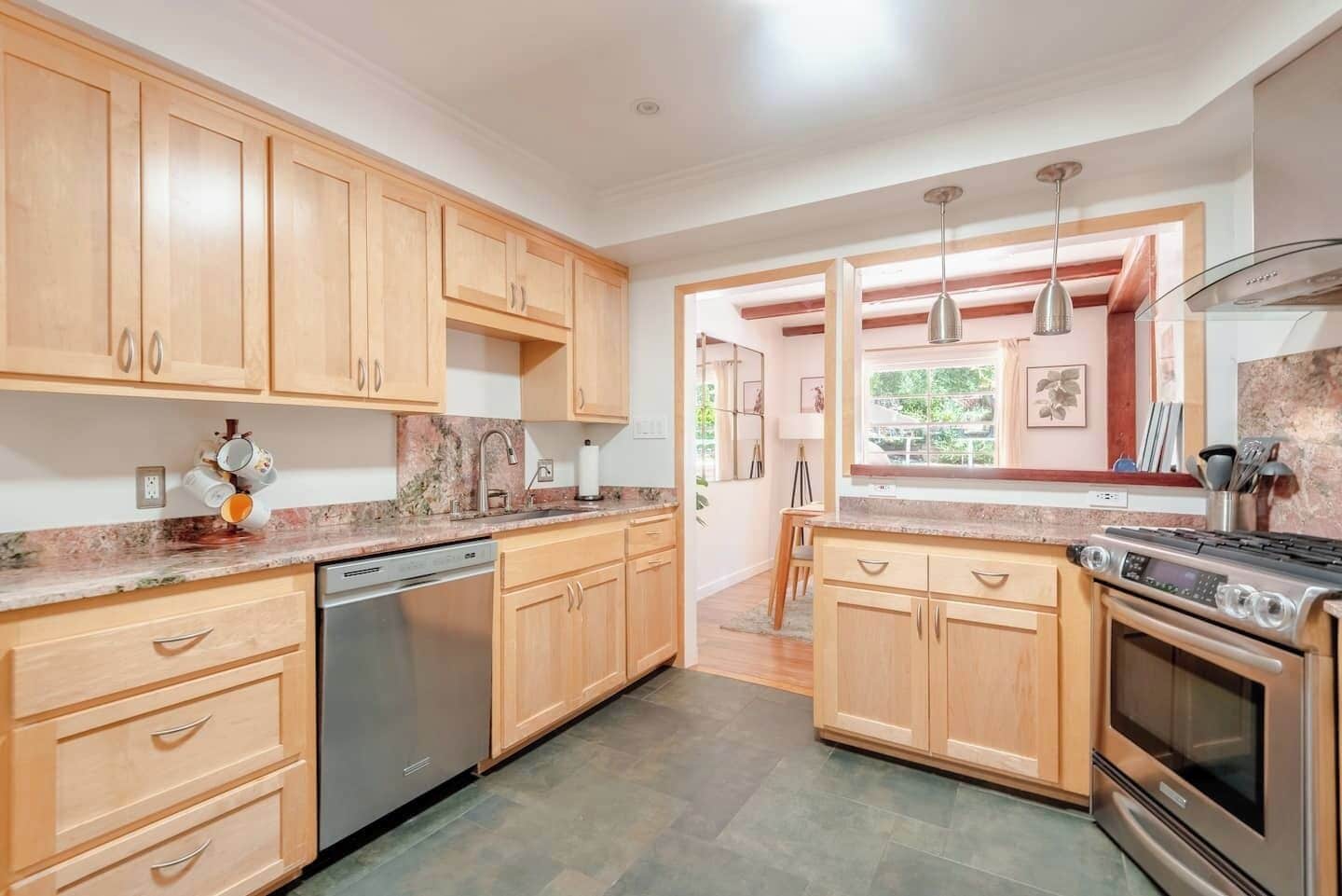 A modern kitchen with wooden cabinets, a dishwasher, a stove, and a window with a view.