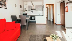 Una cocina moderna con armarios grises, horno empotrado y un comedor con sofá rojo y sillas grises.