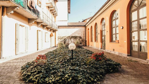 Un patio con una escultura esférica, un camino de ladrillo y edificios con ventanas y puertas de arco.