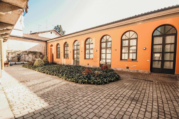 A building with a brick-paved courtyard, arched windows, and a door with a sign.
