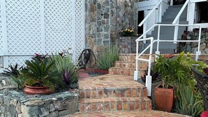 A brick pathway leading to a staircase with a stone wall on one side and a white lattice fence on the other. - Secluded Oceanfront Villa with pool and incredible view! Welcome to Paradise! (St John)
