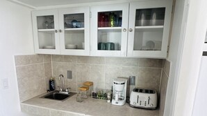 A compact kitchen with a sink, a coffee maker, a toaster, and cabinets containing dishes and glasses. - Secluded Oceanfront Villa with pool and incredible view! Welcome to Paradise! (St John)