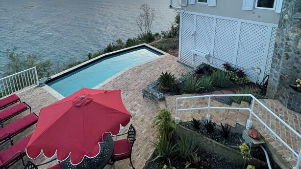 A swimming pool with red chairs and an umbrella, a stone wall, and a view of the sea. - Secluded Oceanfront Villa with pool and incredible view! Welcome to Paradise! (St John)