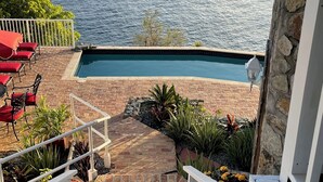 A pool area with a view of the sea, a brick staircase, and outdoor seating. - Secluded Oceanfront Villa with pool and incredible view! Welcome to Paradise! (St John)