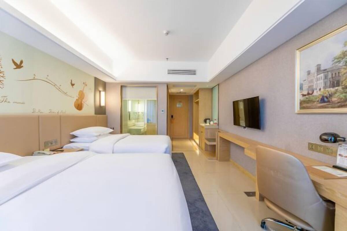 A hotel room with two beds, a desk, a chair, a television, and artwork on the walls.