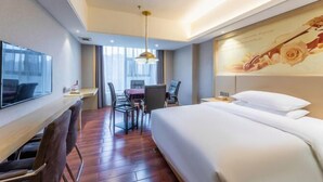 A hotel room with a bed, a desk with a chair, a TV, and a painting on the wall. - Vienna International Hotel (Changsha Orange Isle Head) (Changsha)