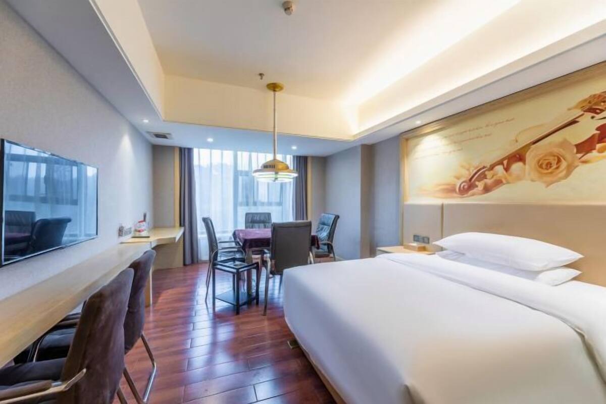A hotel room with a bed, a desk with a chair, a TV, and a painting on the wall.