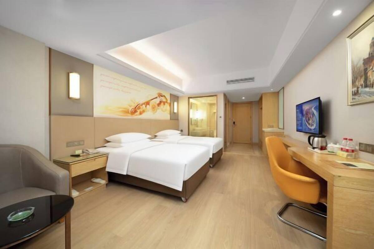 A hotel room with two beds, a desk, a chair, a small table, and a painting on the wall.