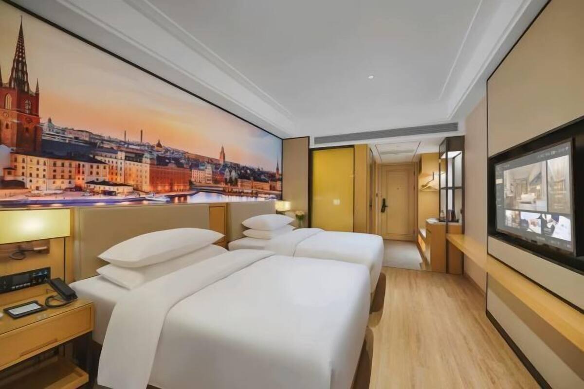 A hotel room with two beds, a large cityscape mural, a television, and a wooden floor.