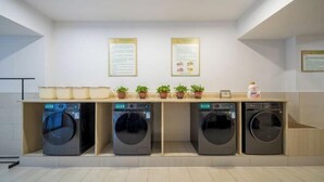 A laundry area with four washing machines, a wooden counter with potted plants, and informational posters on the wall. - Vienna International Hotel (Changsha Orange Isle Head) (Changsha)