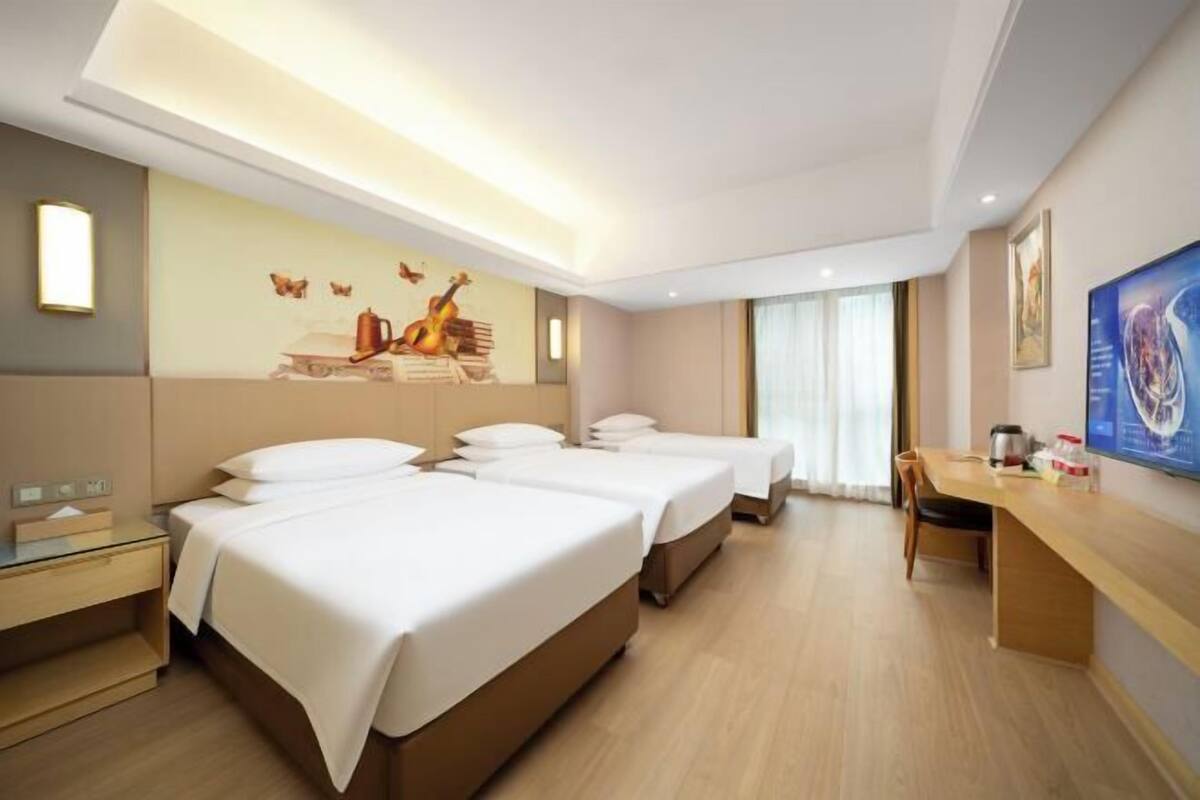 A hotel room with three beds, a desk, and a large window.