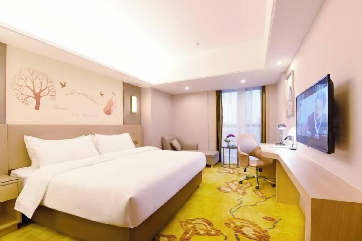 A hotel room with a bed, a desk, a chair, a TV, and a window with curtains.