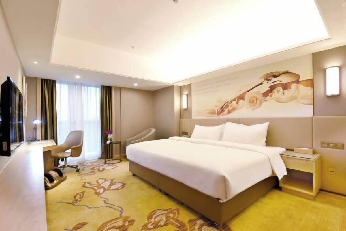 A hotel room with a large bed, a desk, a chair, and a TV.