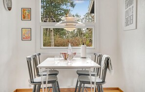 Een eetruimte met een witte tafel, twee stoelen, een hanglamp en een raam met uitzicht op bomen.